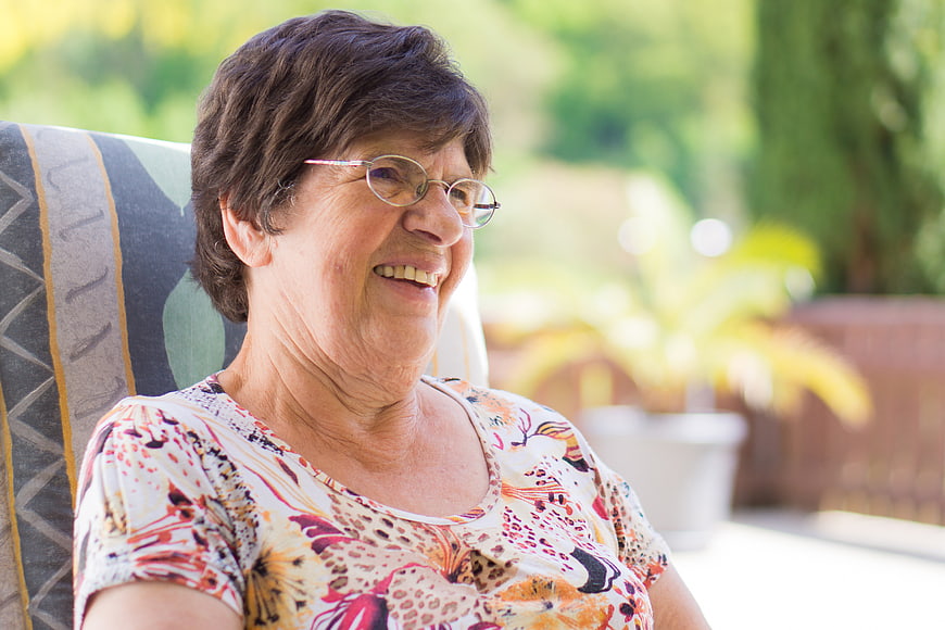 Smiling Senior Woman with Glasses Sitting Outdoors