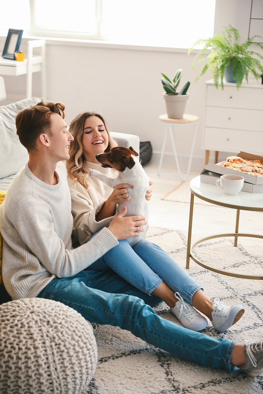 Happy couple relaxing at home with dog and pizza