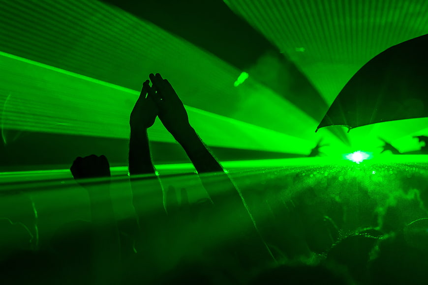 Silhouette of hands raised in green laser light at nightclub