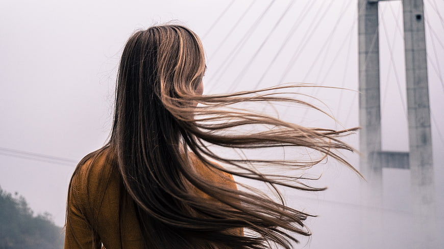 Woman with Windblown Hair Standing Near Bridge
