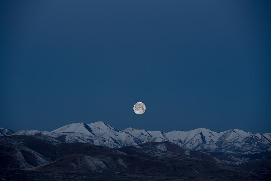 Full Moon Rising Over Snow-Capped Mountain Range at Night
