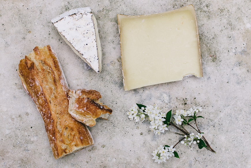 Flat lay of artisanal bread, cheese, and white flowers on concrete