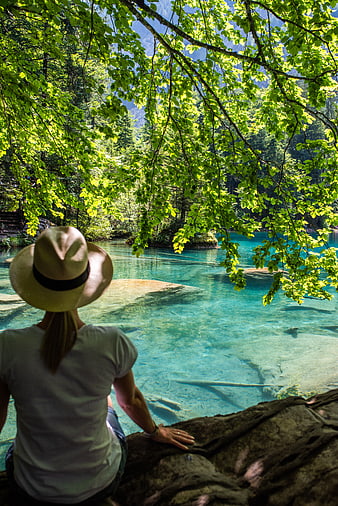 Woman in Hat Sitting by Turquoise River in Forest