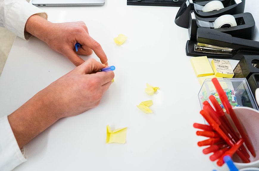 Hands writing on yellow sticky notes at white office desk
