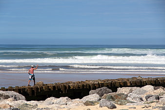 Man standing on rocky breakwater at ocean beach with waves