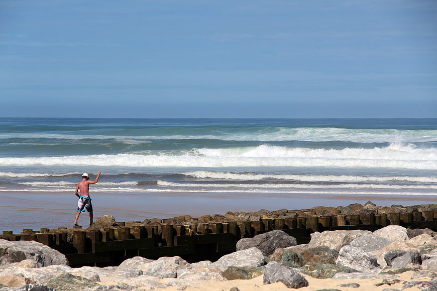 Man standing on rocky breakwater at ocean beach with waves