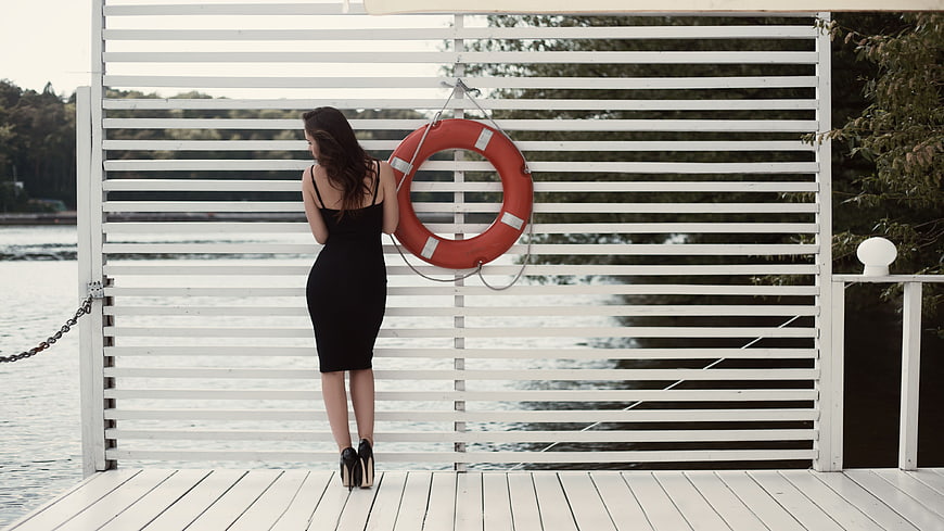 Woman in black dress standing on white wooden dock by lake