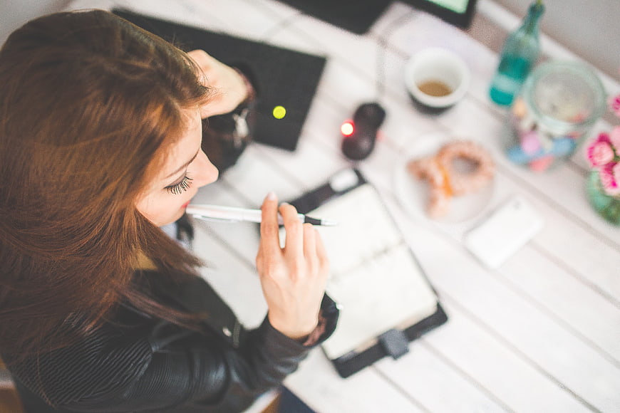 Woman thinking at desk with notebook and coffee