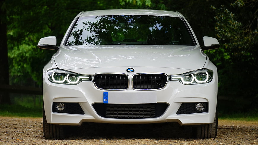 Front view of white BMW sedan in forest