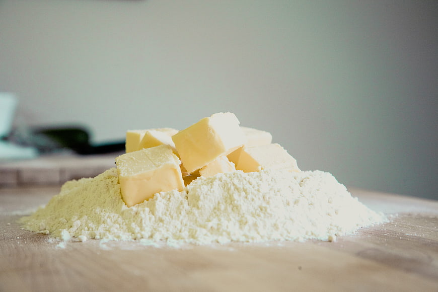 Cubes of butter resting on a pile of white flour on a wooden surface