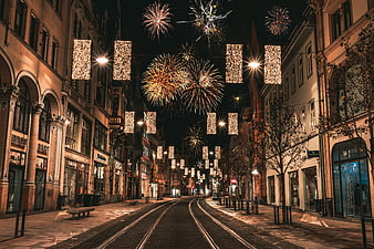 Fireworks over historic European street with festive lights at night