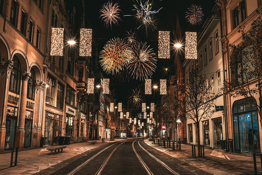 Fireworks over historic European street with festive lights at night
