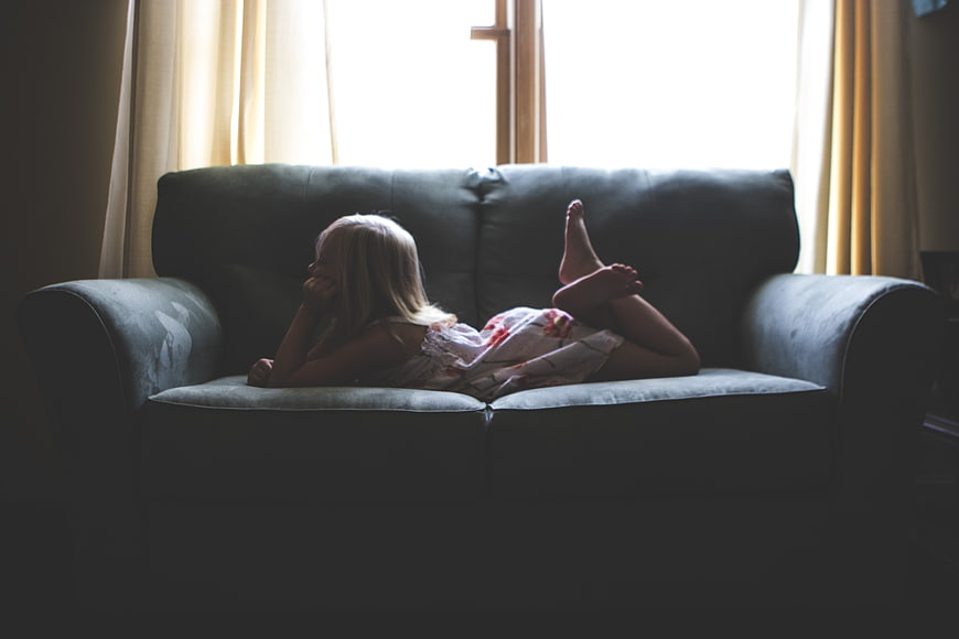 Little girl lying on sofa looking out window