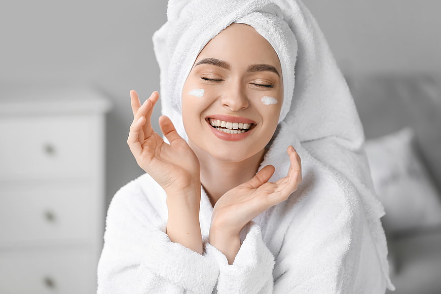 Happy woman with towel on head applying face cream