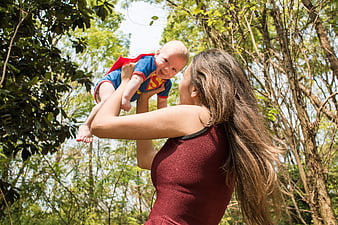 Mother lifting baby in Superman costume in forest