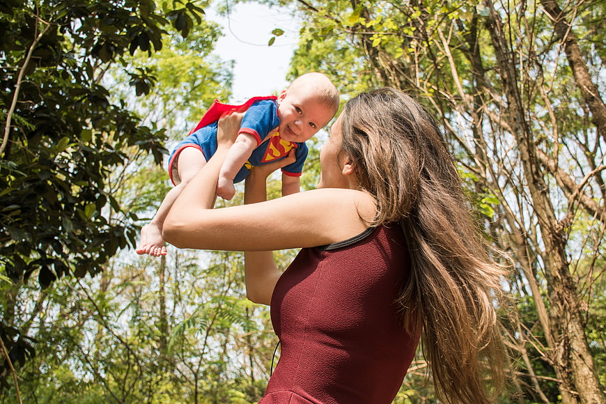 Mother lifting baby in Superman costume in forest