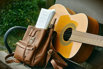 Acoustic guitar and leather backpack with sheet music on bench