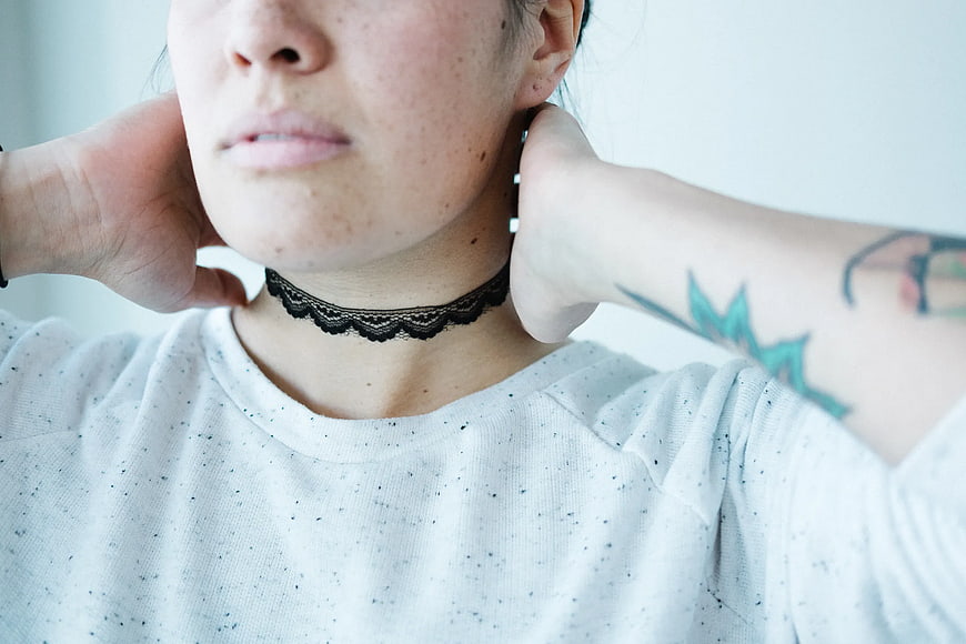 Close-up of woman with black lace choker and arm tattoo