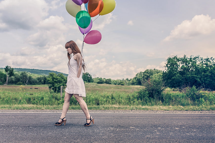 Woman in White Dress Walking on Road with Colorful Balloons