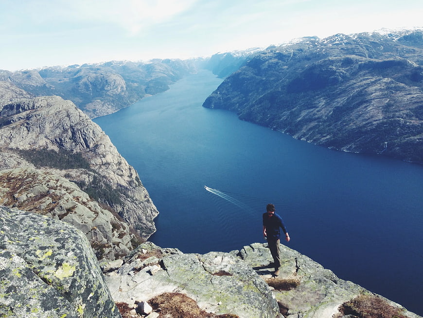 Man standing on rocky cliff overlooking deep blue fjord