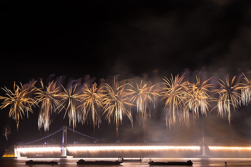 Golden Fireworks Display Over Illuminated Suspension Bridge At Night