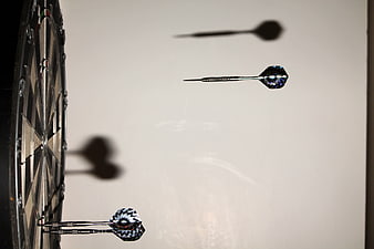 Darts in mid-air with shadows on a wall near a dartboard