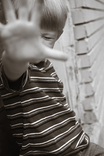 Child holding hand up in stop gesture against brick wall
