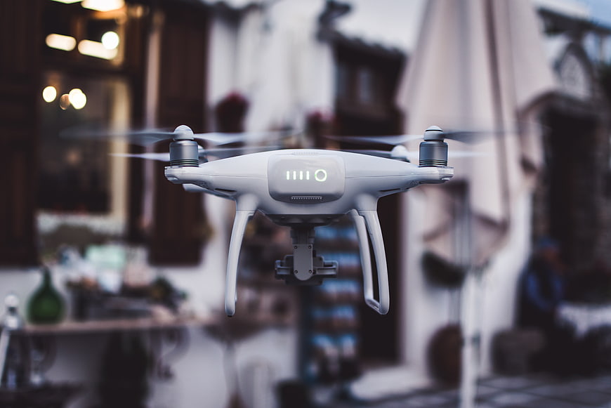 White drone hovering in front of blurred outdoor cafe background