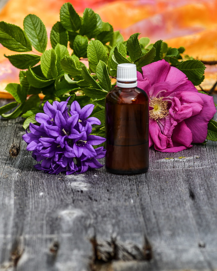 Aromatic Essential Oil Bottle With Purple And Pink Flowers On Rustic Wood