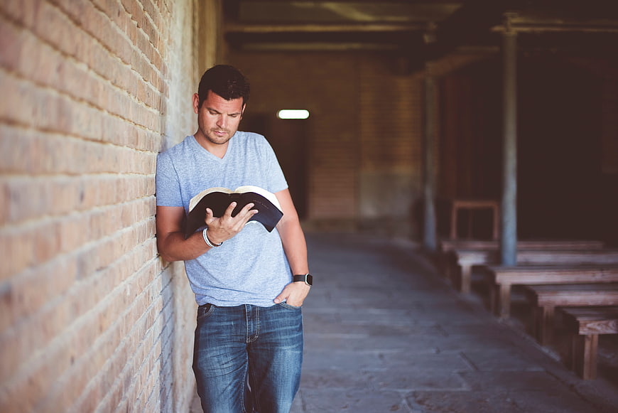 Man reading a book while leaning against a brick wall in a chapel