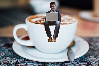 Man working on laptop sitting on giant coffee cup