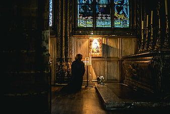 Woman kneeling in prayer before stained glass window in church