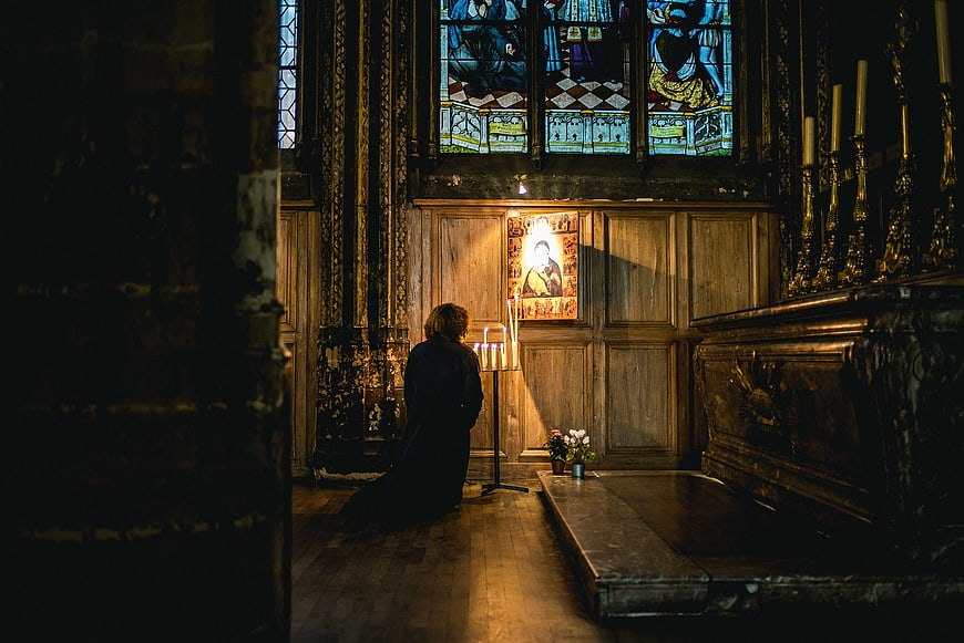 Woman kneeling in prayer before stained glass window in church