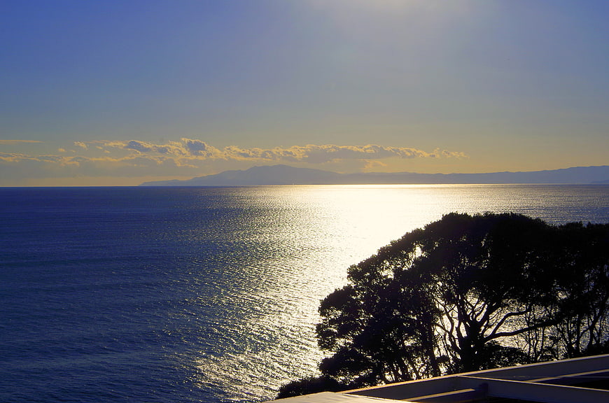 Sunset Ocean View with Silhouette Tree and Distant Mountains