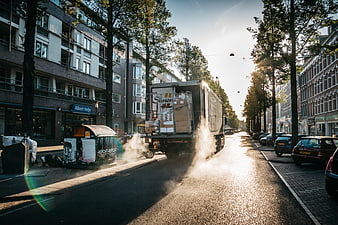 Delivery truck driving down a sunny urban street with smoke
