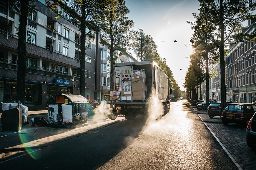Delivery truck driving down a sunny urban street with smoke
