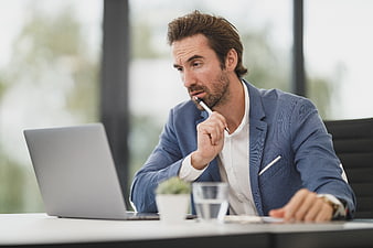 Thoughtful businessman working on laptop in modern office