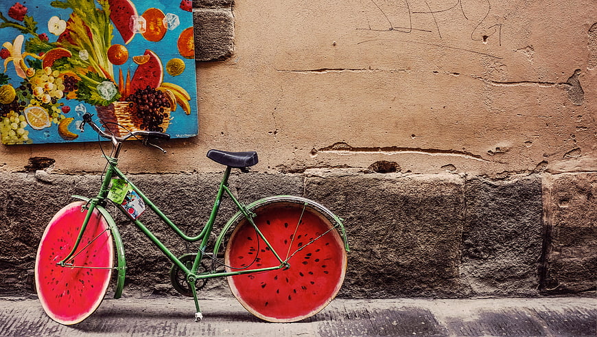 Green bicycle with watermelon wheels against textured wall