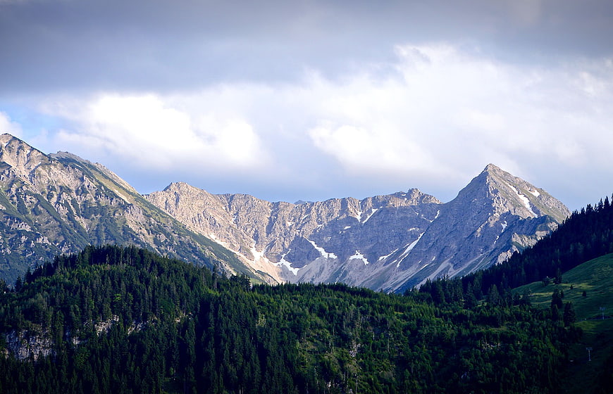 Majestic Mountain Range with Forested Hills and Cloudy Sky