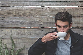 Young man drinking coffee from white cup against wooden wall