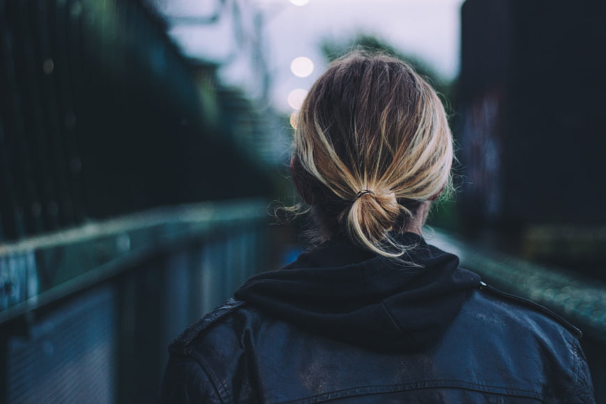 Back view of woman with blonde hair walking on urban bridge