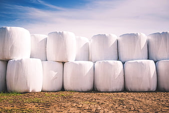 Stack of white hay bales in a field under blue sky
