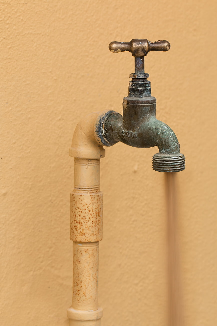 Rusty outdoor faucet on beige wall