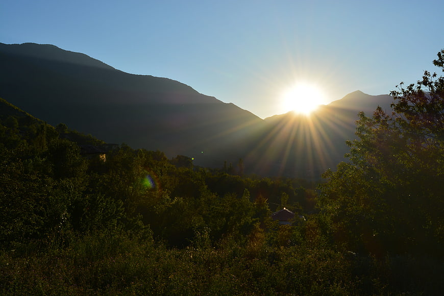 Sunburst over mountain ridge with lush green forest