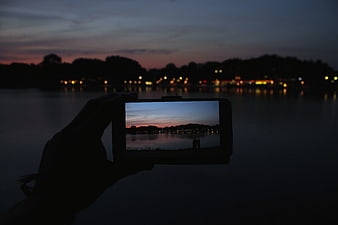 Hand holding smartphone capturing sunset cityscape over water