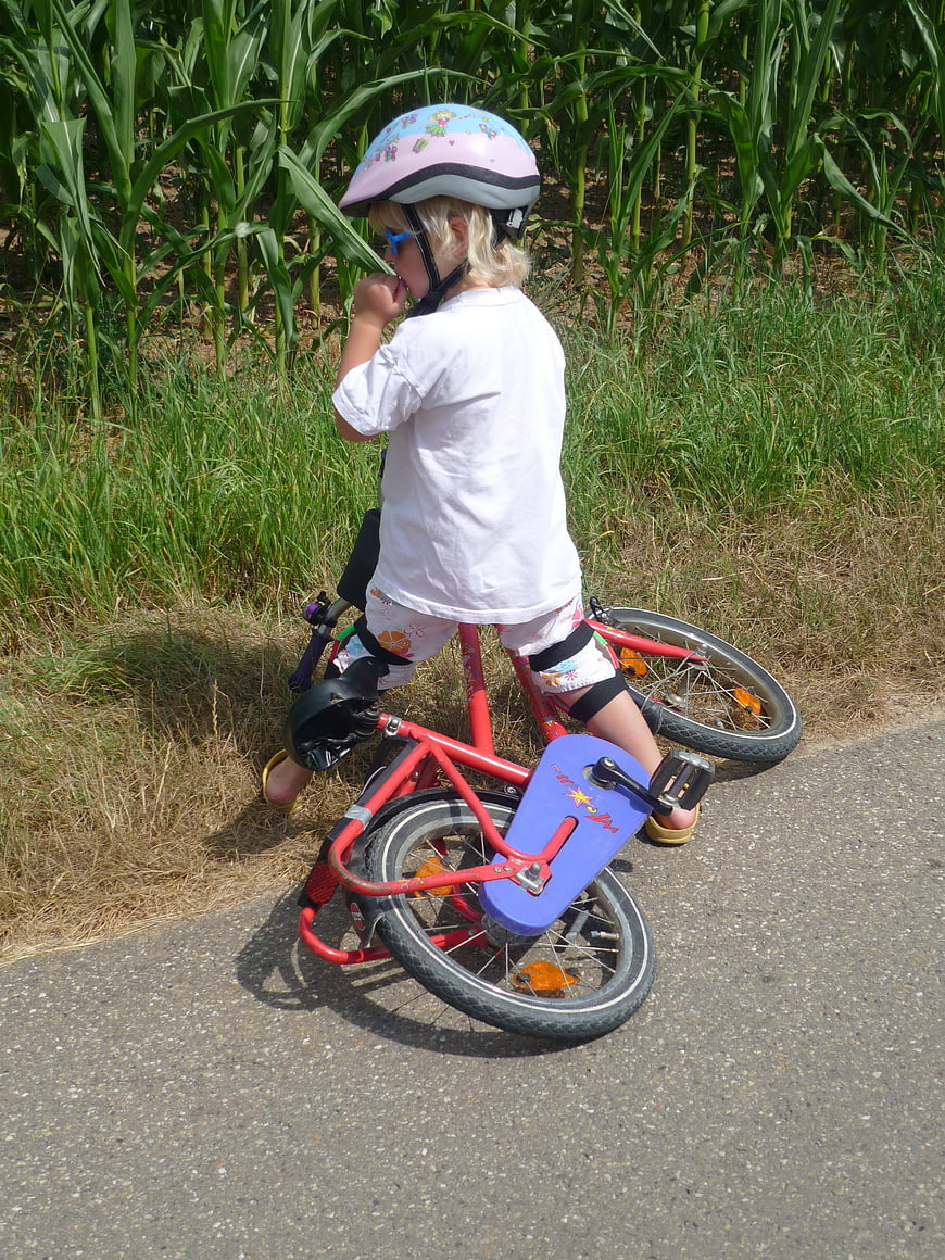 Young child with pink helmet on red balance bike near cornfield