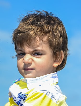 Close-up portrait of an angry toddler boy against blue sky