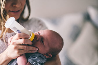 Mother feeding newborn baby with bottle close up