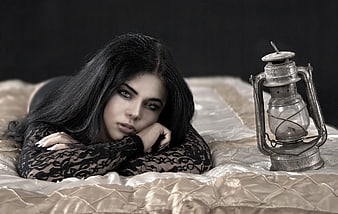 Woman in black lace lying on bed with vintage lantern