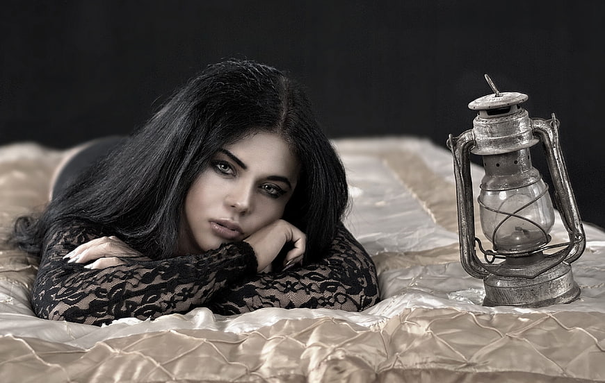 Woman in black lace lying on bed with vintage lantern